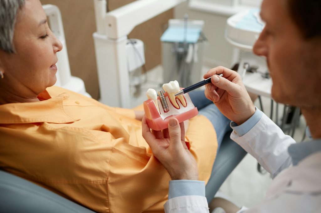 Closeup of male dentist explaining dental implant surgery to patient in clinic